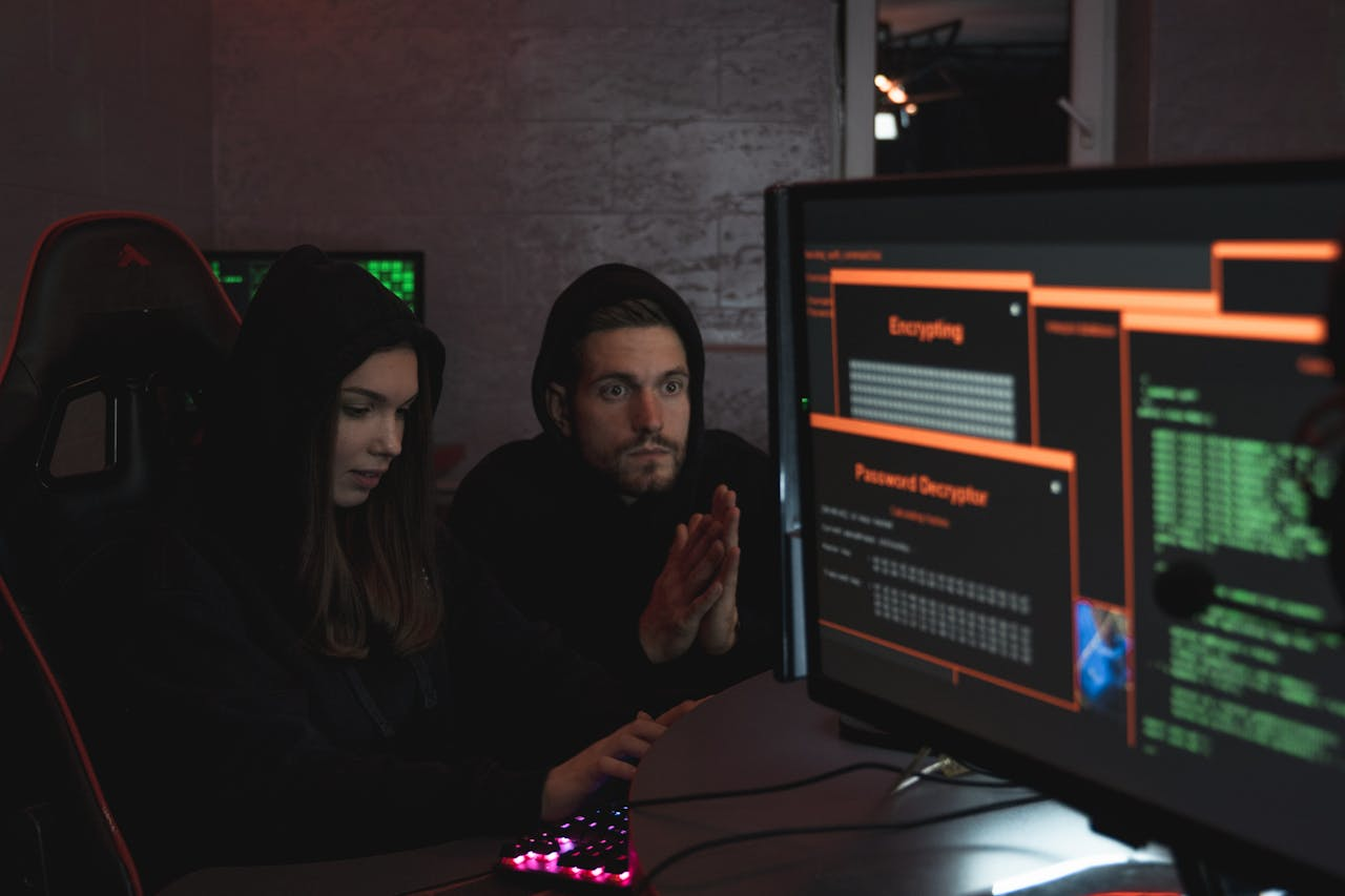 Cybersecurity experts in hoodies analyzing encrypted data on computer screens in an indoor setting.